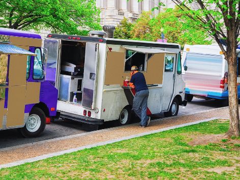 Food trucks lined up on a tree-shaded lawn
