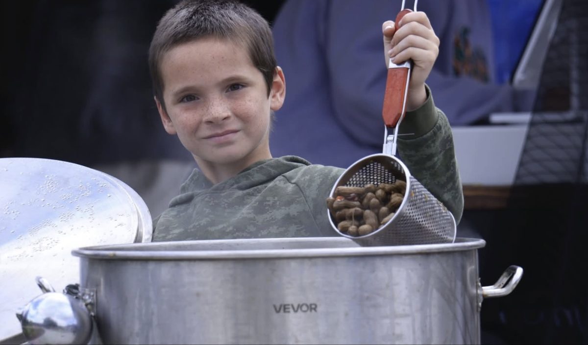 A boy holding up a basket of hot boiled peanuts from a big pot at Zombie Nutz