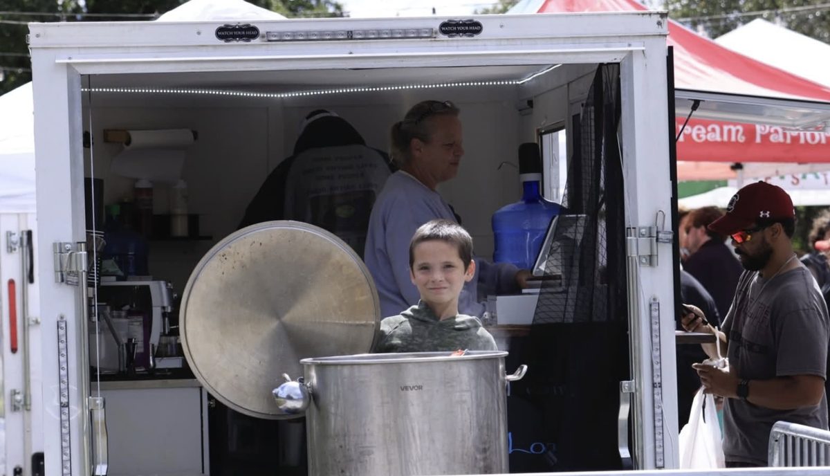 A young helper standing behind a big steaming pot at the Zombie Nutz food trailer
