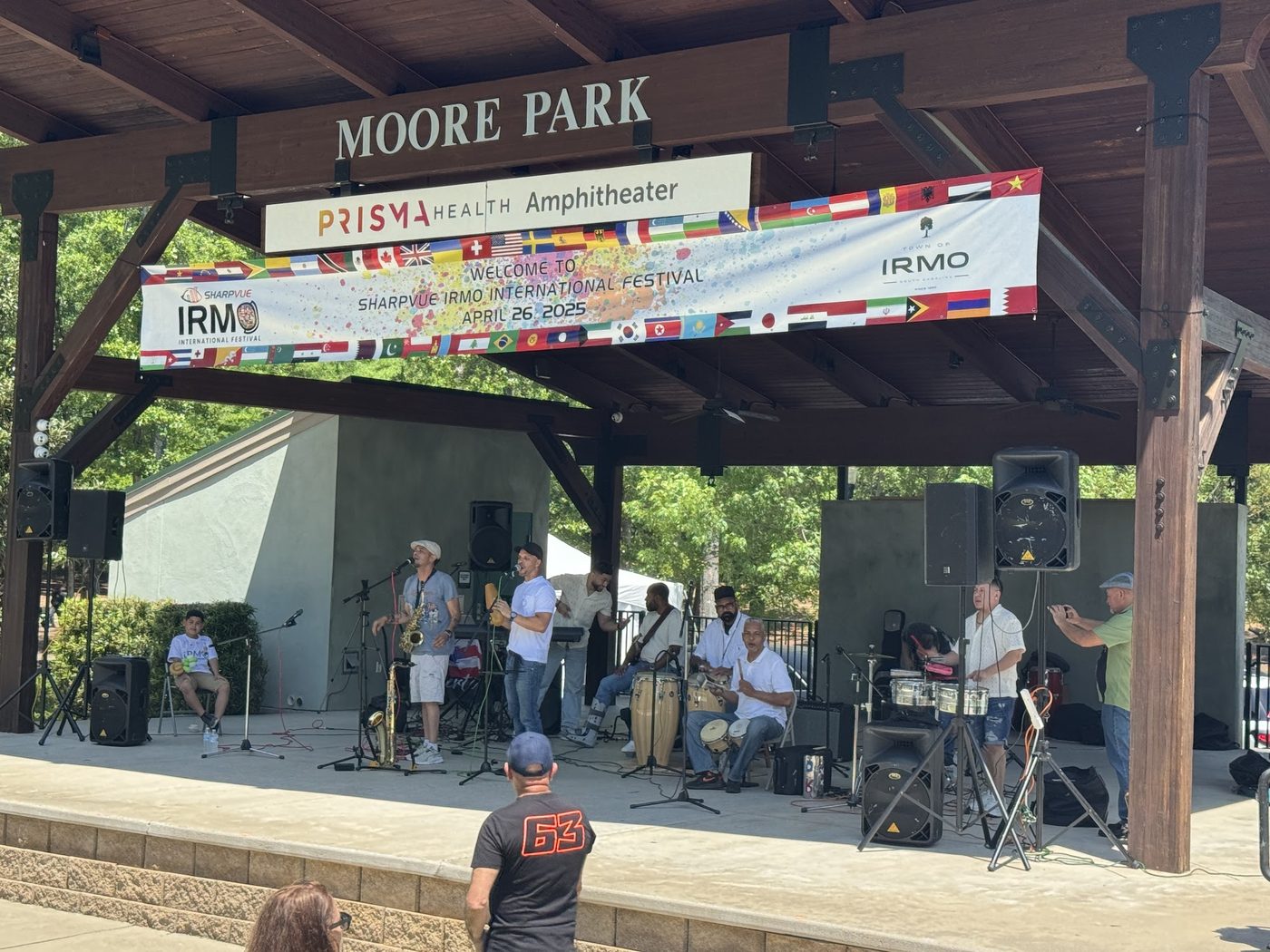 A Latin band with saxophone, congas and timbales performing on the Moore Park stage under the 2025 festival banner